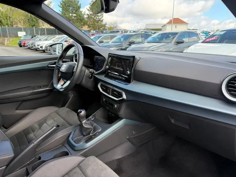 Vue intérieure côté conducteur du SEAT Arona 2025, tableau de bord moderne avec écran tactile et levier de vitesse manuel.