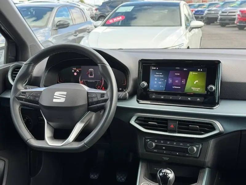 Vue intérieure du tableau de bord et volant du SEAT Arona 2025, avec écran tactile central et commandes au volant.