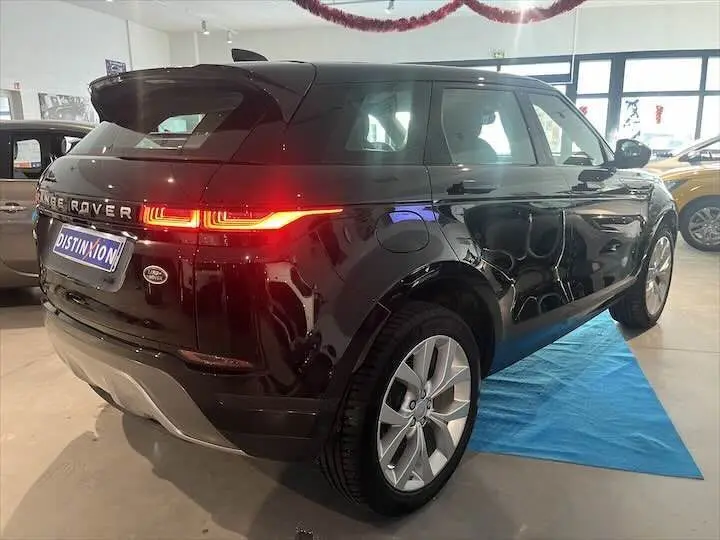 Vue 3/4 arrière droite d'un Range Rover Evoque noir Santorini avec feux arrière allumés en showroom.