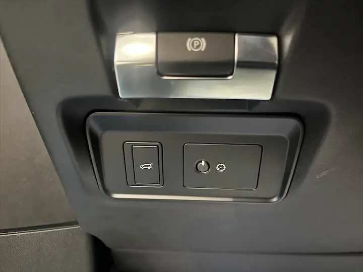 Gros plan sur les commandes intérieures du Range Rover Evoque noir Santorini, avec bouton ouverture hayon et frein à main électrique.