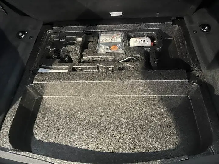 Coffre ouvert du Range Rover Evoque noir Santorini, montrant le rangement intégré sous le plancher avec outils et kit de secours.