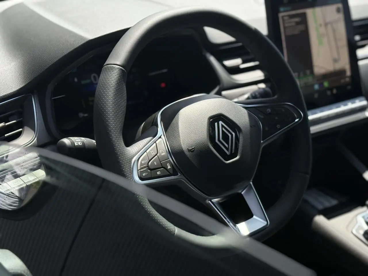 Gros plan sur le volant cuir multifonctions du Renault Captur 2025, avec tableau de bord et écran tactile en arrière-plan.