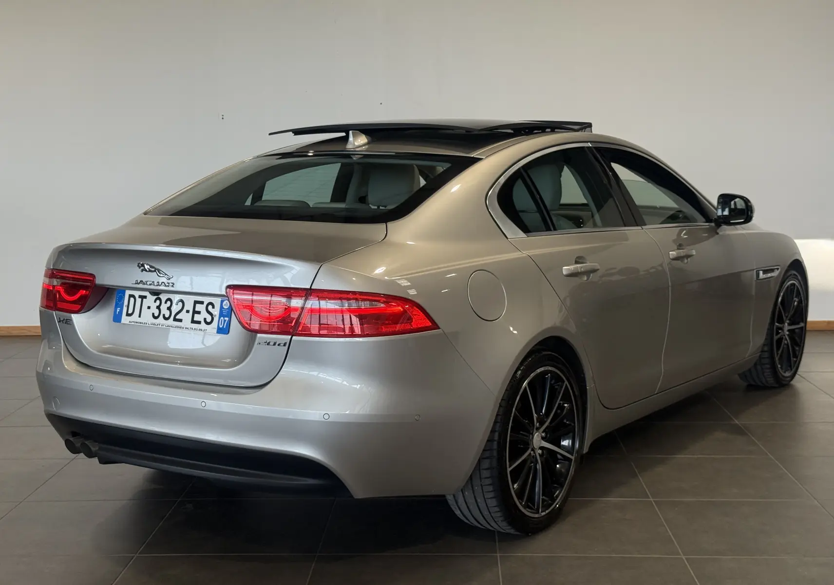 Vue 3/4 arrière droite d'une Jaguar XE beige 2015 avec jantes noires et toit ouvrant panoramique.