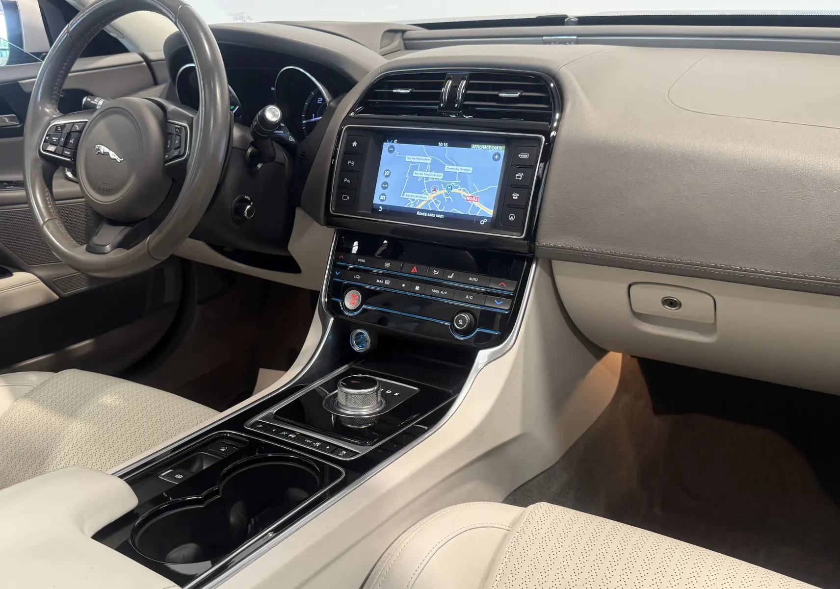 Intérieur beige clair de la Jaguar XE 20d Prestige 2015, vue côté conducteur sur tableau de bord et console centrale avec écran tactile.