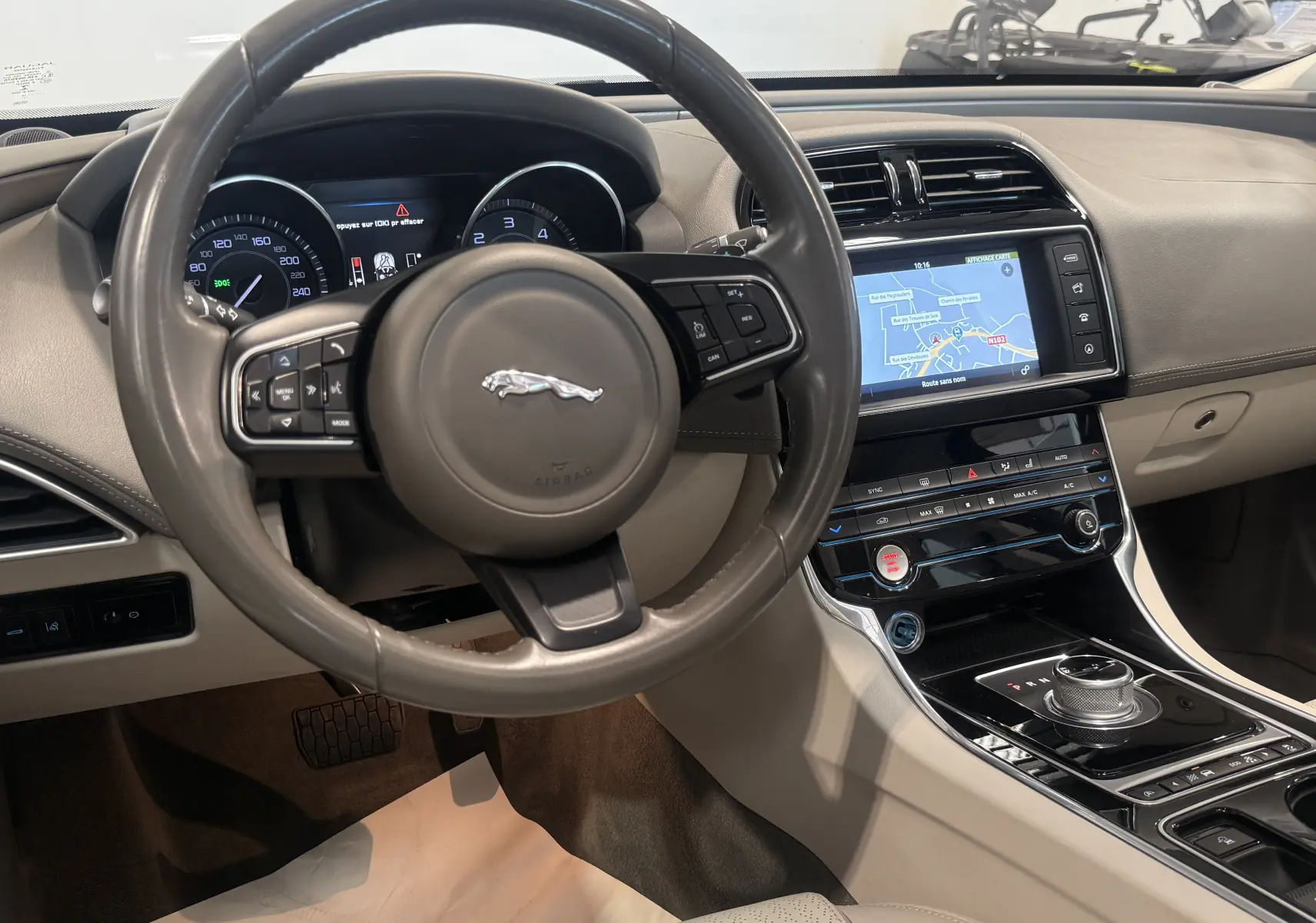 Intérieur beige du Jaguar XE 20d 2015 vu côté conducteur, avec volant multifonction et écran tactile de navigation.