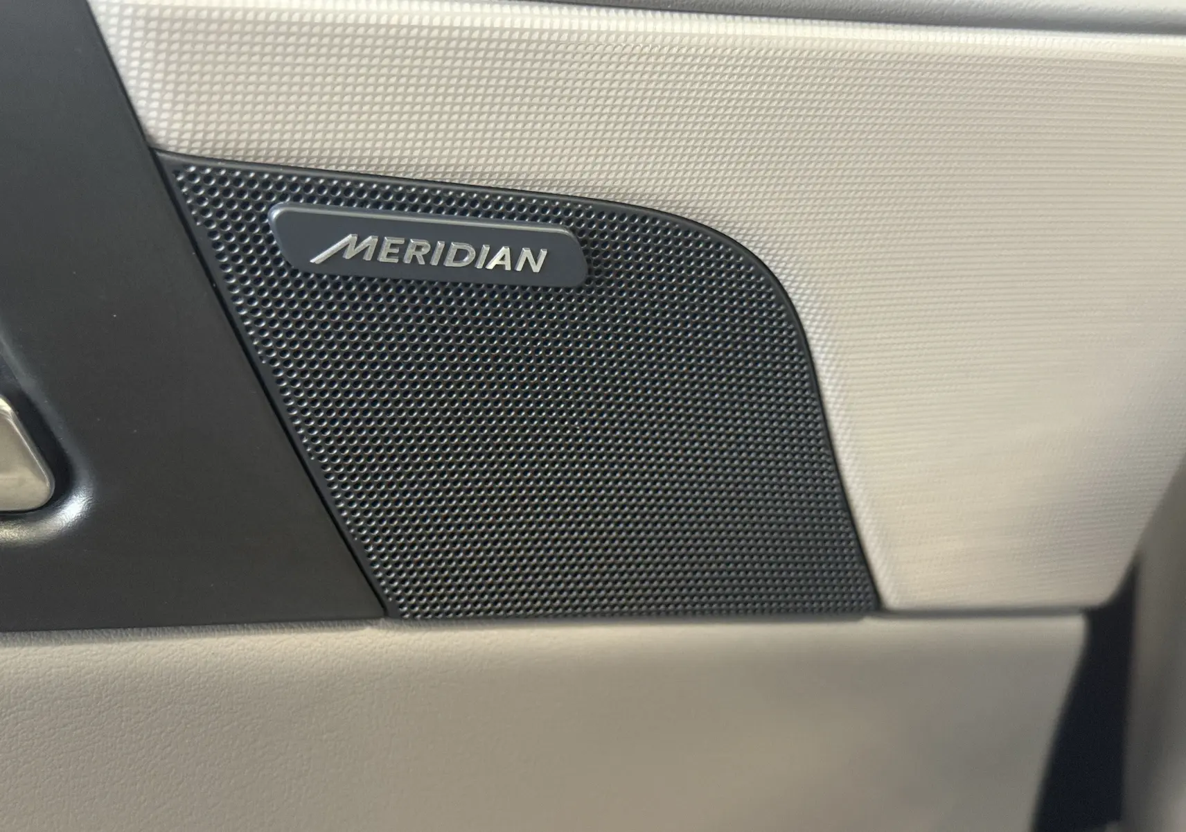 Gros plan sur l'enceinte Meridian intégrée à la porte beige intérieure de la Jaguar XE 20d Prestige 2015.