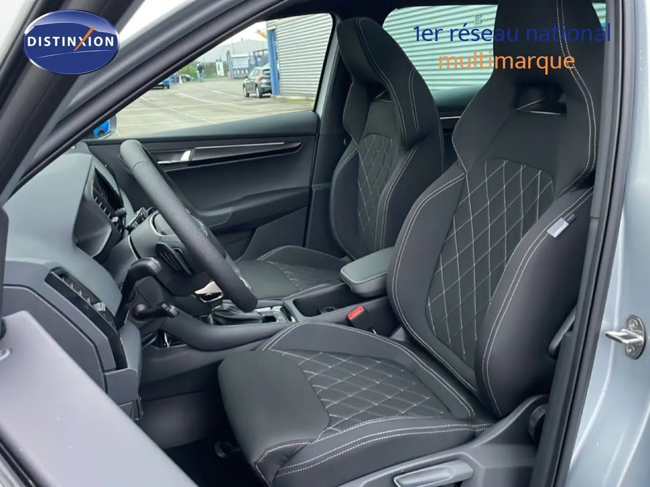 Intérieur avant du Skoda Karoq gris argent 2025, sièges sport noirs avec surpiqûres blanches et volant cuir multifonction.