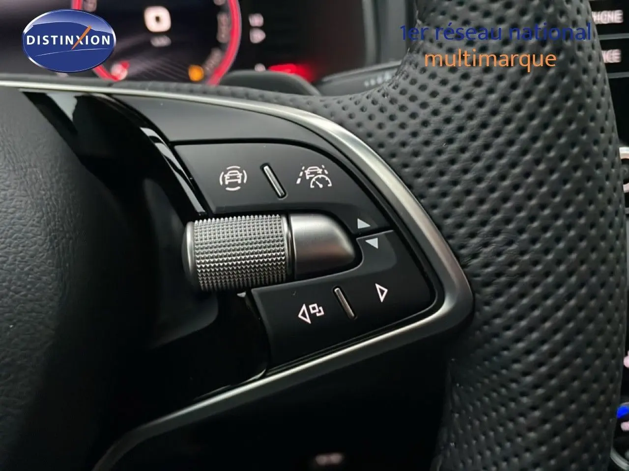 Gros plan sur les commandes au volant perforé du Skoda Karoq gris argent 2025, avec affichage numérique en arrière-plan.