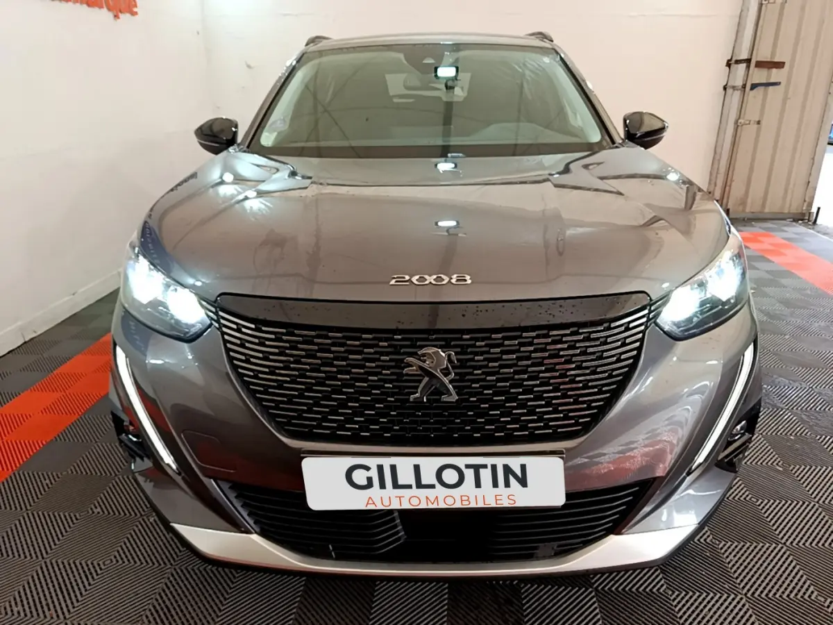 Vue frontale d'un Peugeot 2008 gris foncé avec calandre noire et phares LED allumés en intérieur showroom.