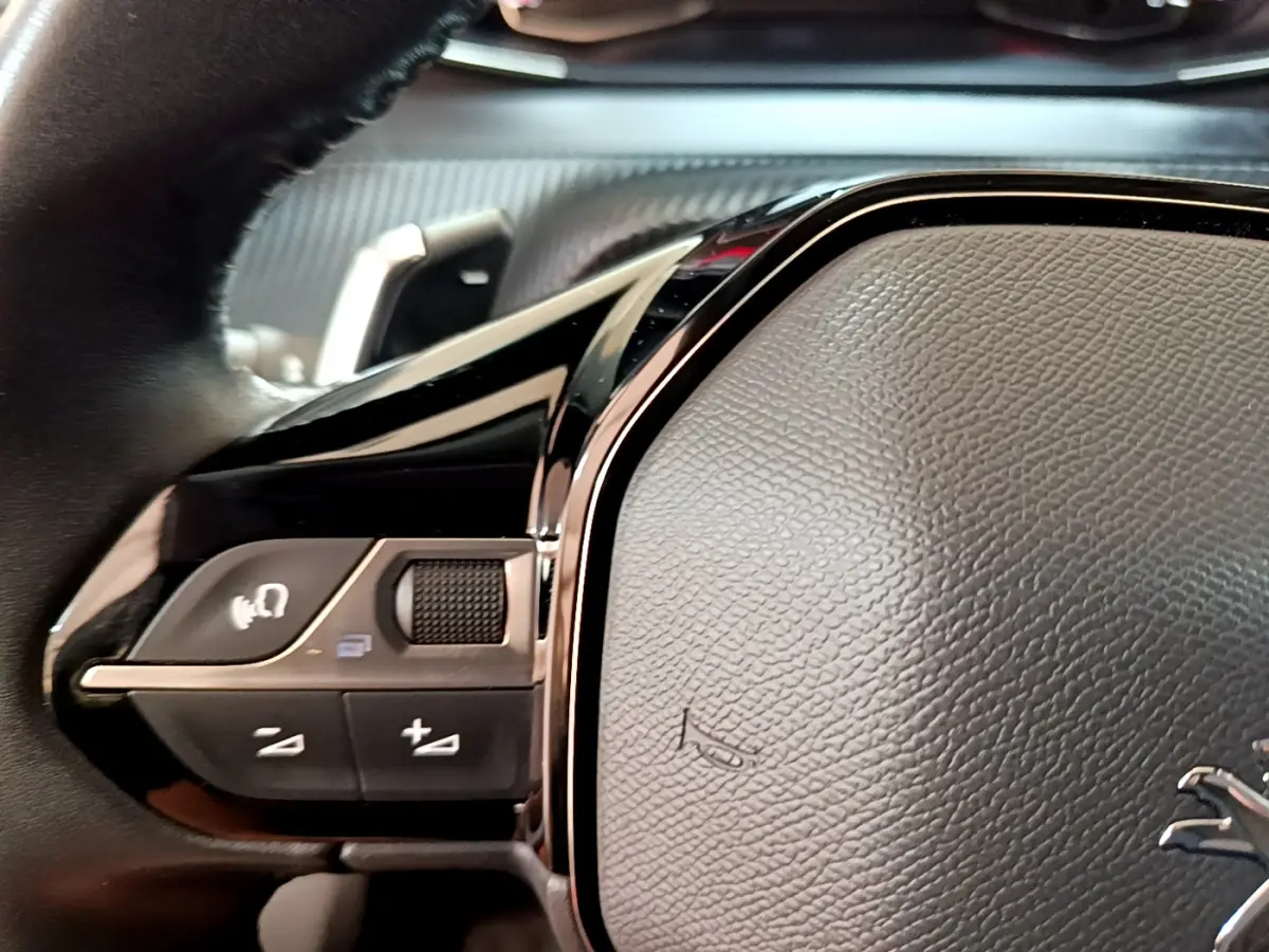 Gros plan sur le volant cuir multifonctions noir du Peugeot 2008 gris foncé, avec commandes intégrées visibles.
