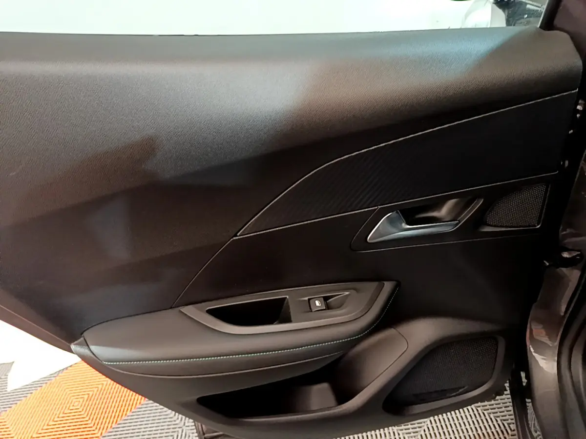 Vue intérieure côté gauche de la porte avant d'une Peugeot 2008 gris foncé avec garniture noire et poignée argentée.