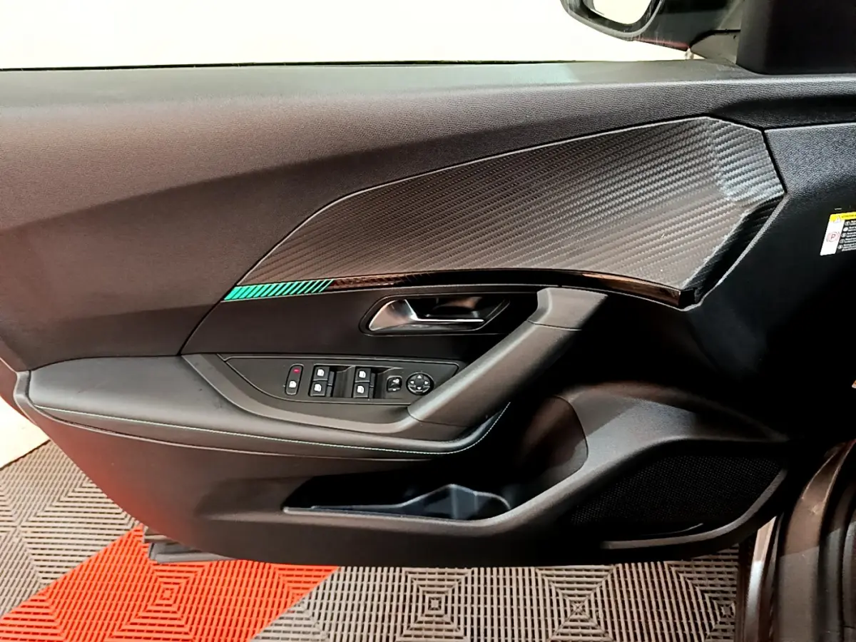 Vue intérieure côté gauche de la porte d'une Peugeot 2008 gris foncé, avec garniture carbone et commandes électriques.