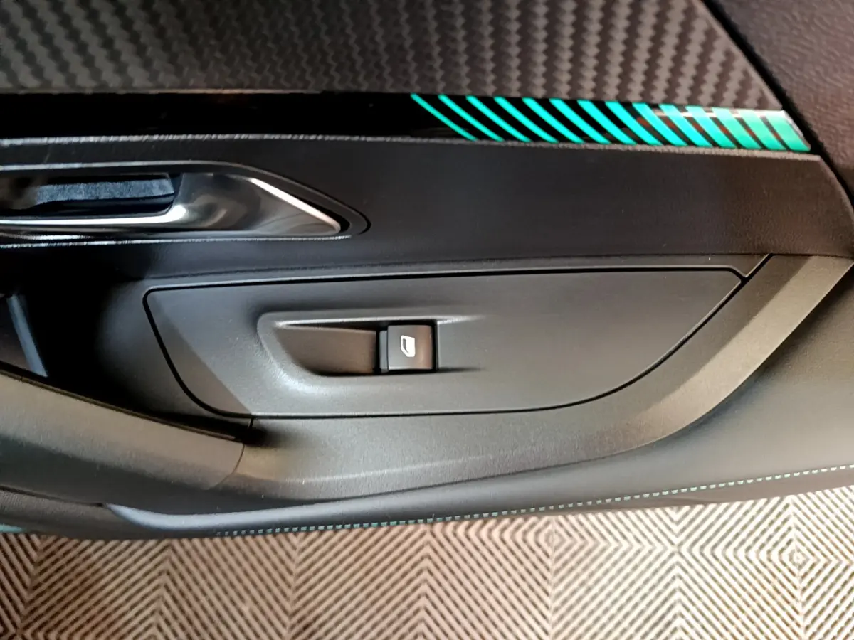 Détail de la porte intérieure côté gauche d'une Peugeot 2008 gris foncé, avec bouton de lève-vitre et insert décoratif bleu.