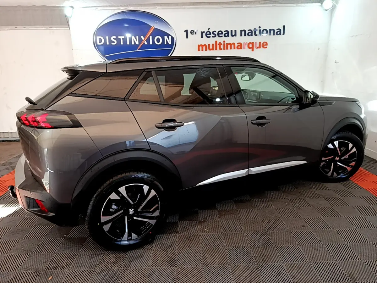 Vue côté droit d’un Peugeot 2008 gris foncé 2022 avec jantes noires et toit noir dans un showroom.