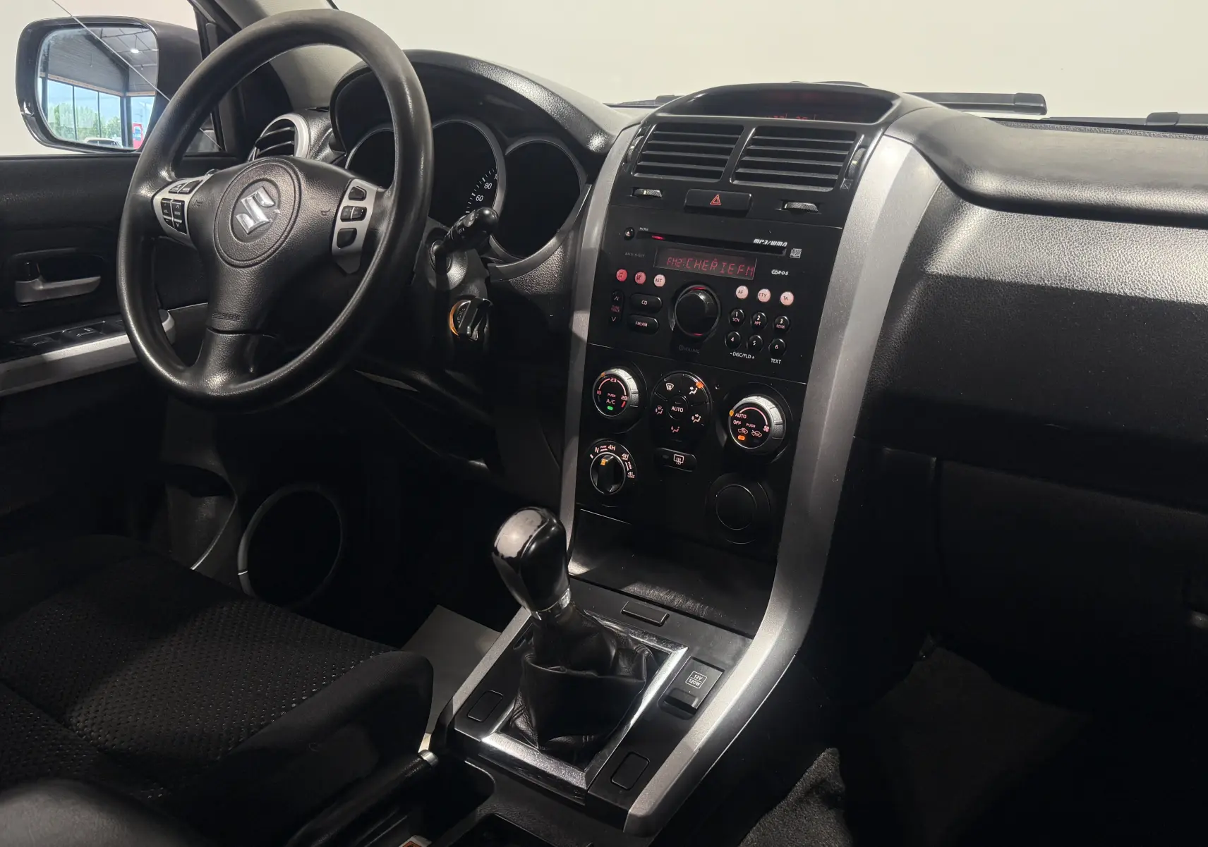 Intérieur du Suzuki Grand Vitara 2007 gris, vue du tableau de bord côté conducteur avec levier de vitesses manuel.