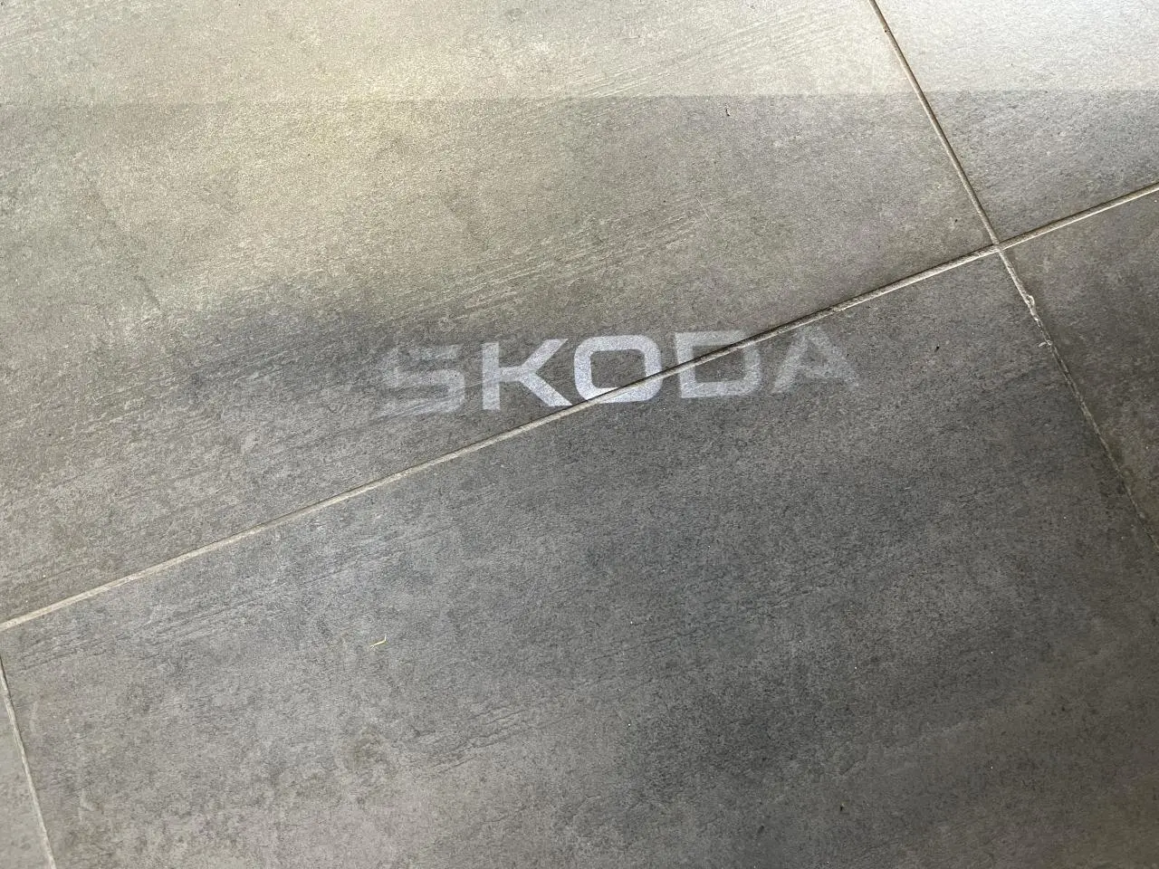 Projection lumineuse du logo SKODA au sol sur un carrelage gris, sans véhicule visible.