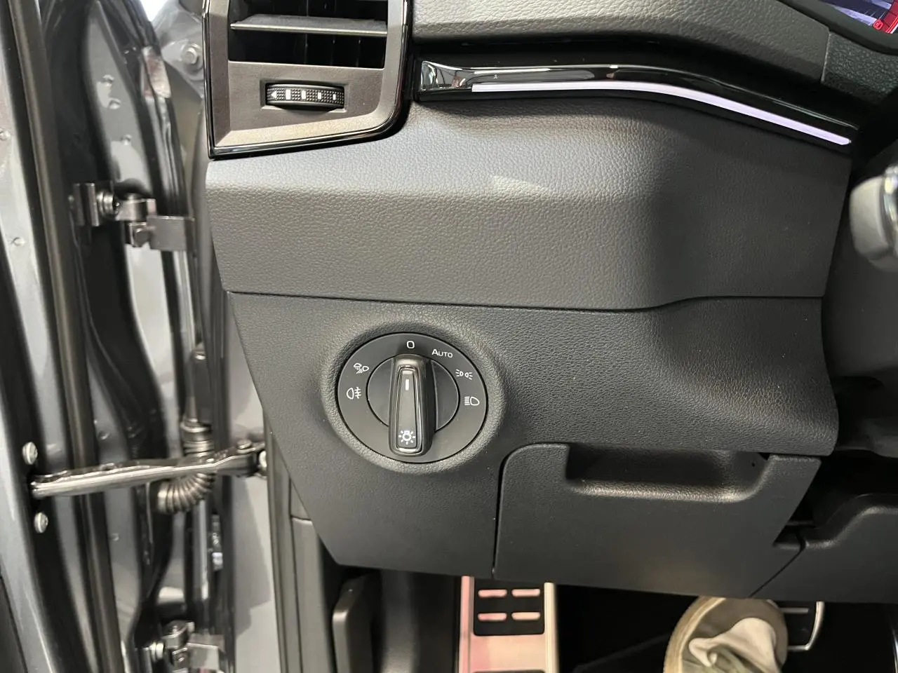 Gros plan sur le bouton de commande des phares côté gauche du tableau de bord d'un Skoda Karoq gris 2025 Sportline.