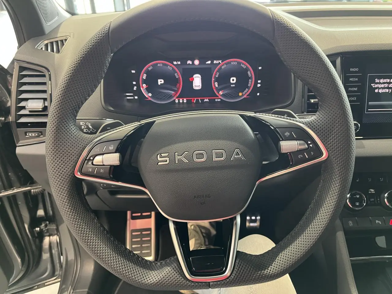 Vue rapprochée du volant perforé SKODA avec tableau de bord digital rouge et console centrale noire du KAROQ 2025 Sportline.