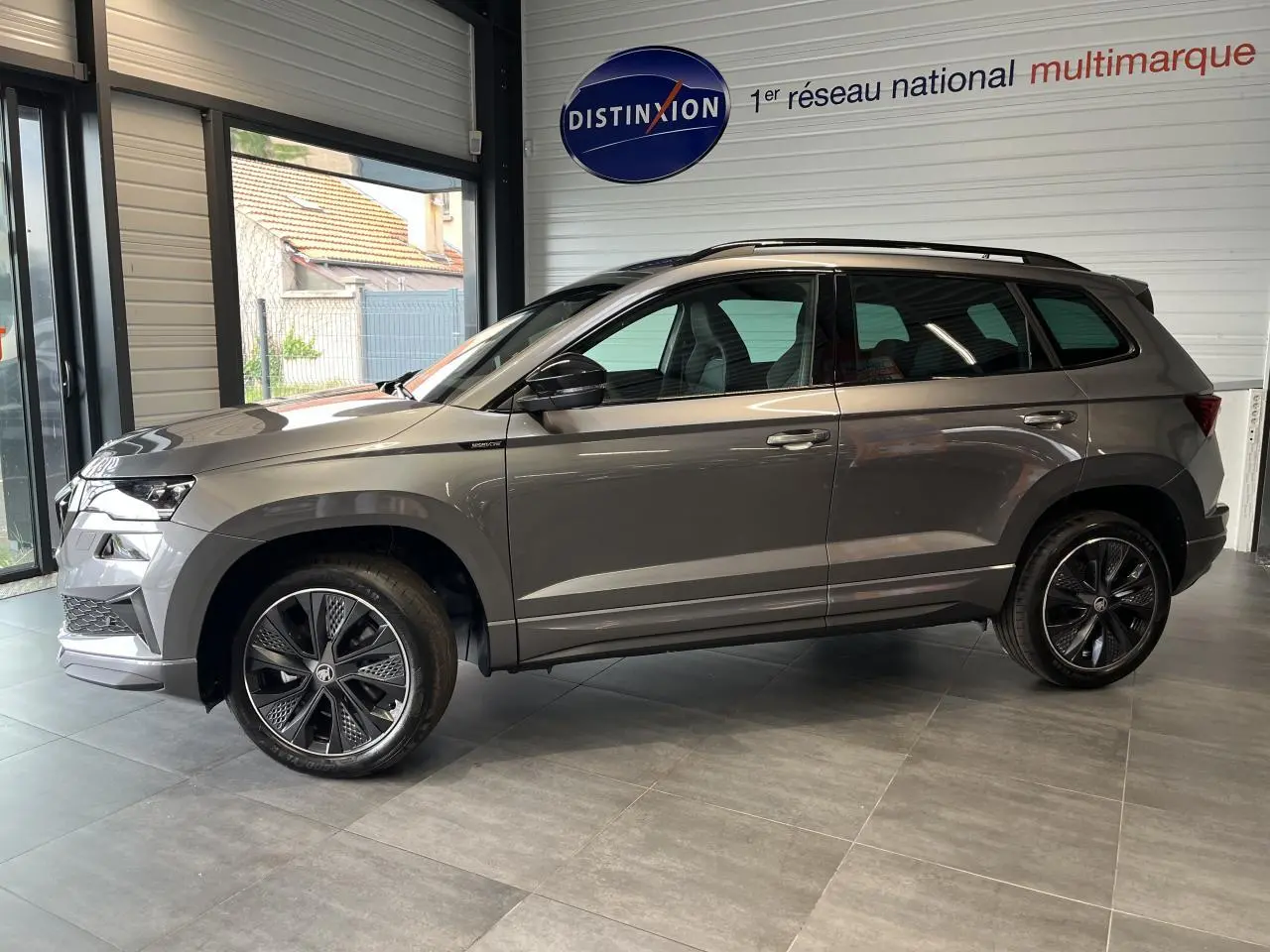 SUV SKODA KAROQ gris en profil droit dans un showroom avec jantes alliage noires et toit ouvrant noir.
