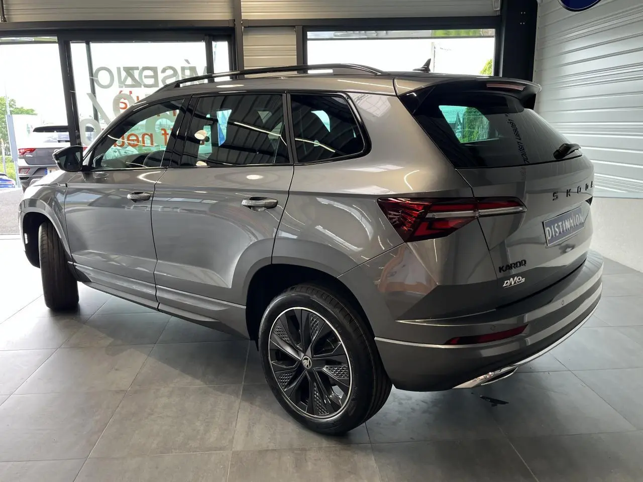 Vue 3/4 arrière droite du SUV SKODA KAROQ gris métallisé avec jantes alliage 19'' Sagitarius anthracite et toit noir.
