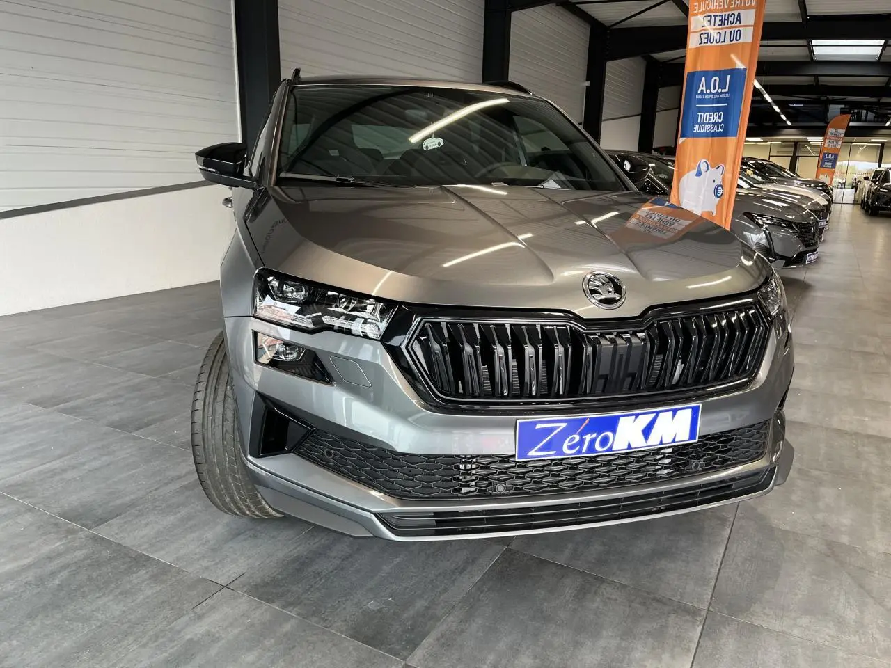 Vue avant rapprochée du SUV SKODA KAROQ gris métallisé avec calandre noire et phares LED en showroom.