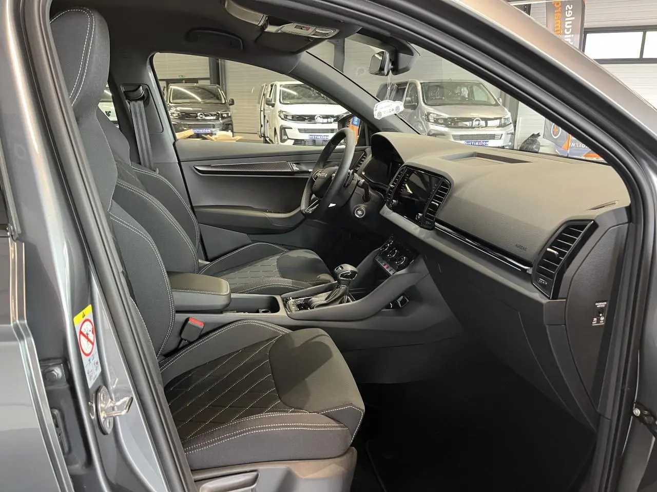 Intérieur avant droit du Skoda Karoq gris 2025, sièges sport noirs avec surpiqûres blanches et tableau de bord moderne.