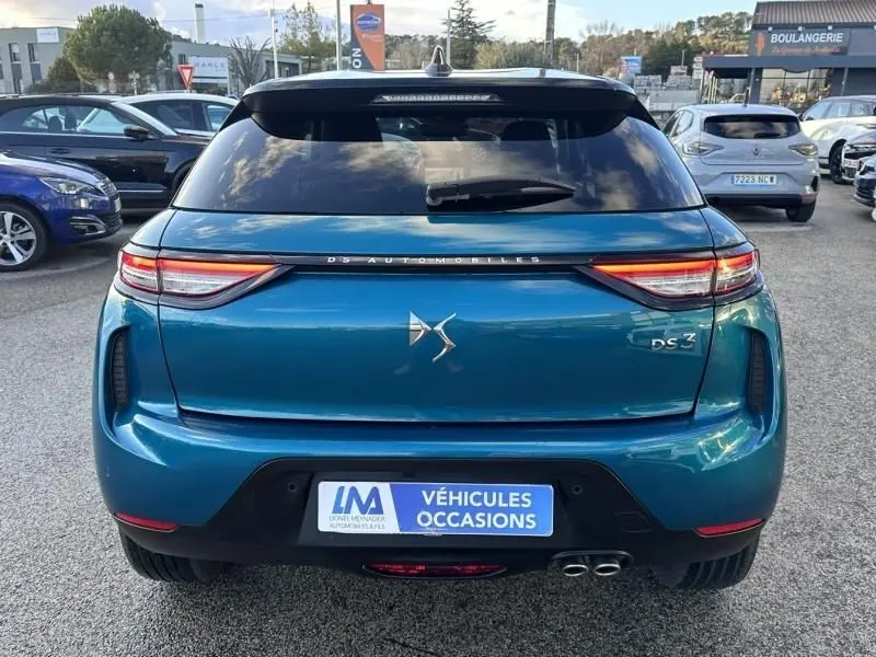 Vue arrière d'une DS3 1.2 Hybride 145 Étoile bleu métal 2025 avec feux allumés et double sortie d'échappement visible.