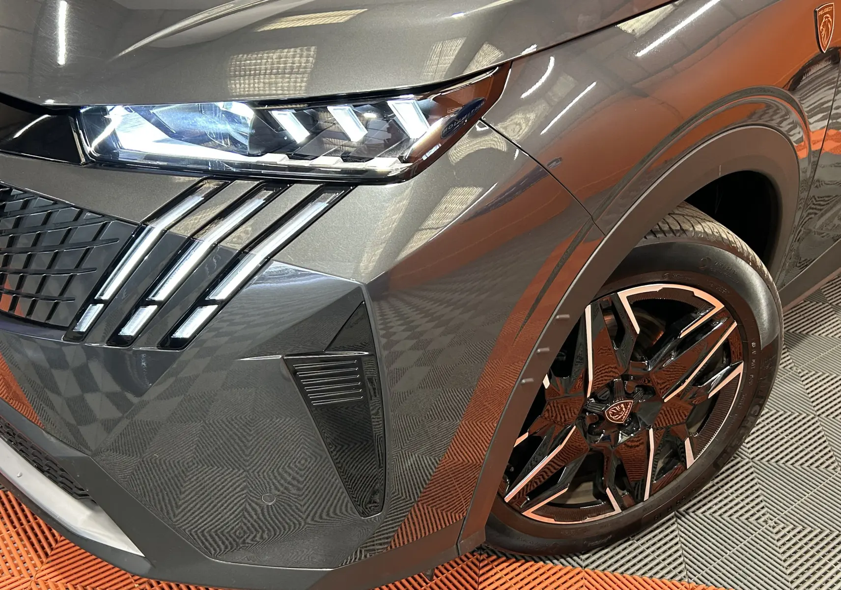 Gros plan sur l’avant droit du Peugeot 5008 gris titane, mettant en valeur le phare LED et la jante noire à inserts métallisés.