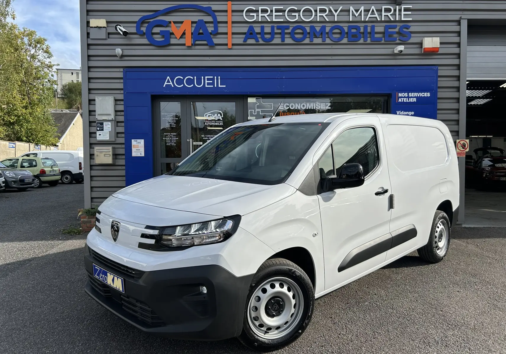 Fourgon blanc Peugeot Partner BlueHDi 2025 vu en 3/4 avant droit devant un garage GMA.