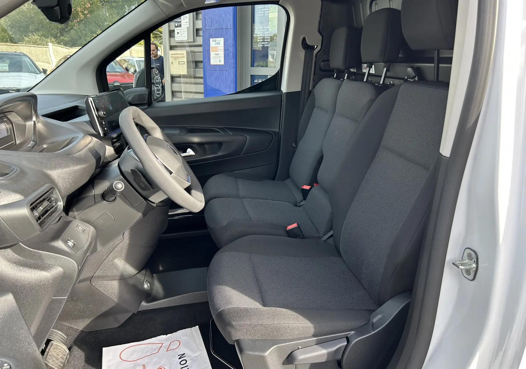 Intérieur côté conducteur du Peugeot Partner Fourgon blanc 2025, banquette 3 places en tissu gris et tableau de bord moderne.