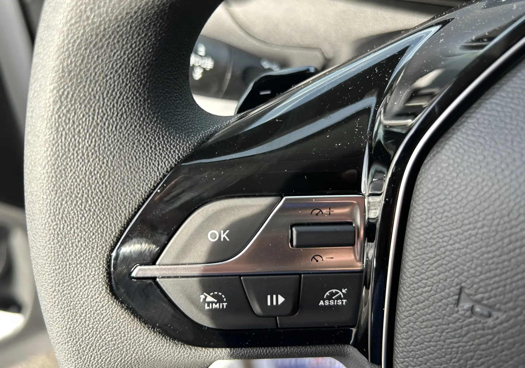 Gros plan sur les commandes du volant noir du Peugeot Partner Fourgon blanc, avec boutons de limitation et assistance.