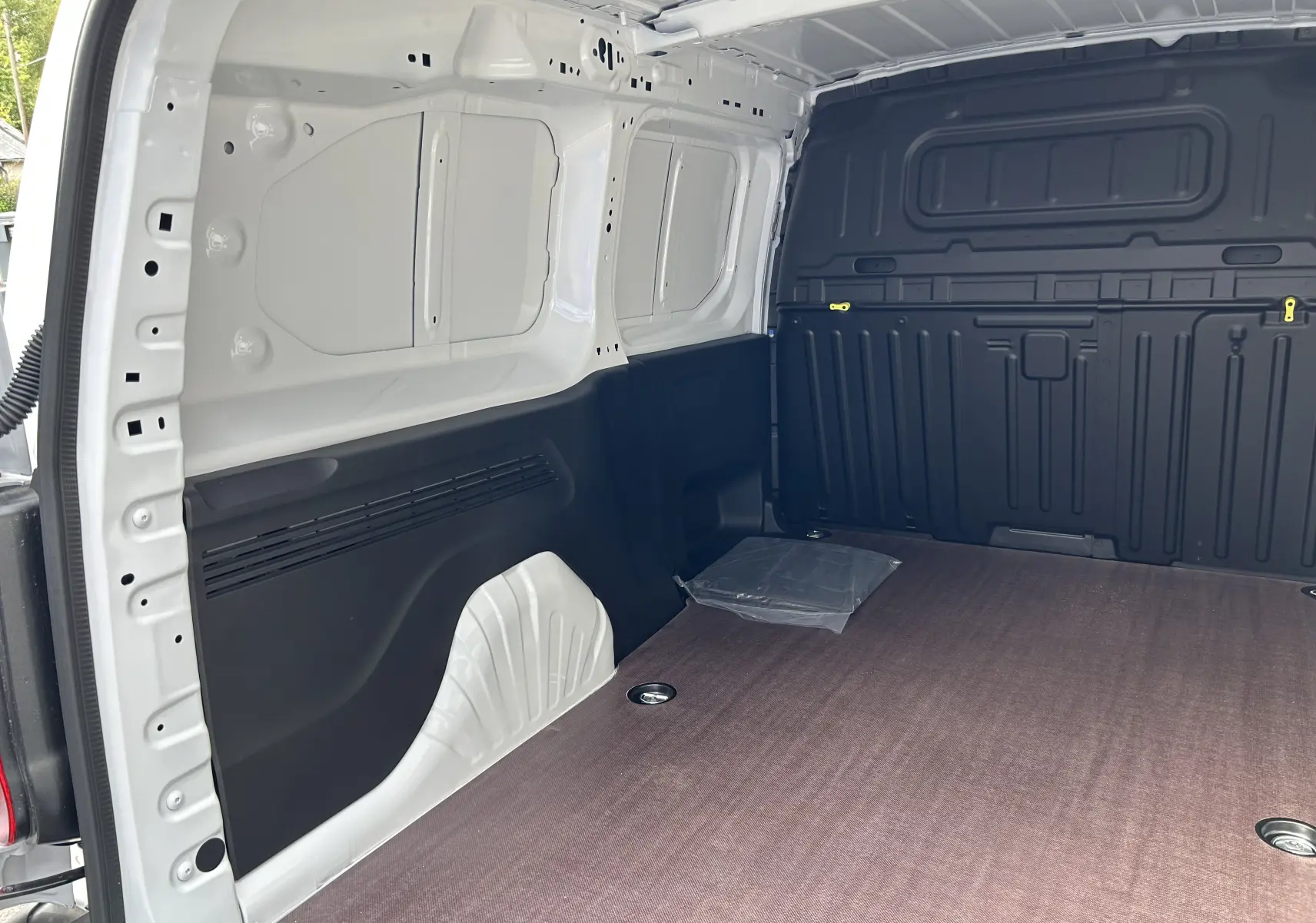 Intérieur du fourgon Peugeot Partner blanc vu de l'arrière, plancher bois et parois noires visibles.