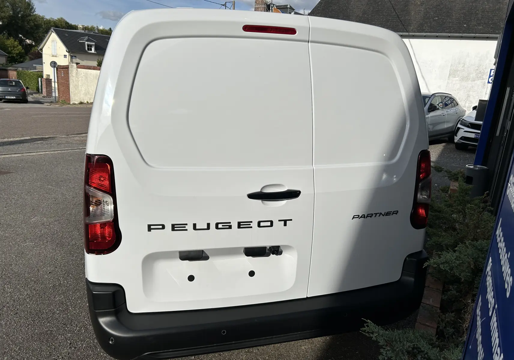 Vue arrière d'un Peugeot Partner Fourgon blanc avec logo noir et feux arrière rouges sur parking extérieur.