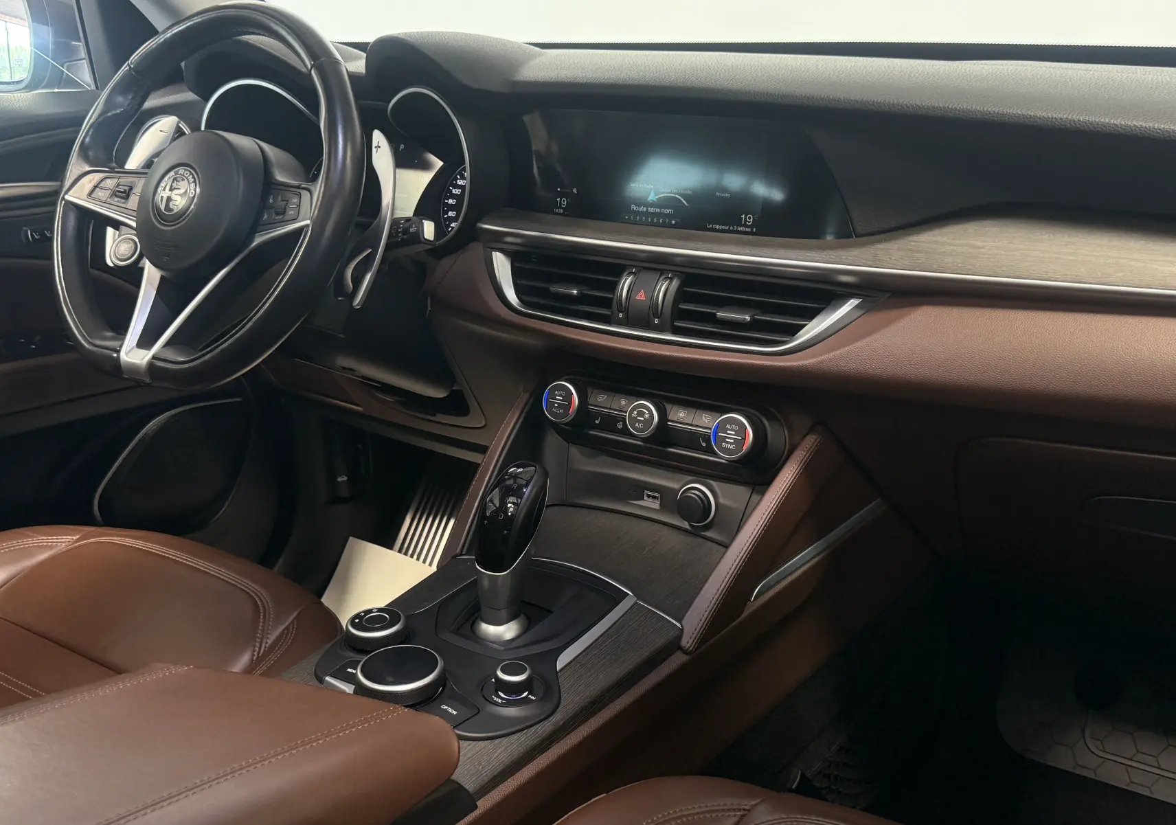 Intérieur de l'Alfa Romeo Stelvio 2017 vu côté conducteur, avec sellerie marron et tableau de bord moderne gris et bois.