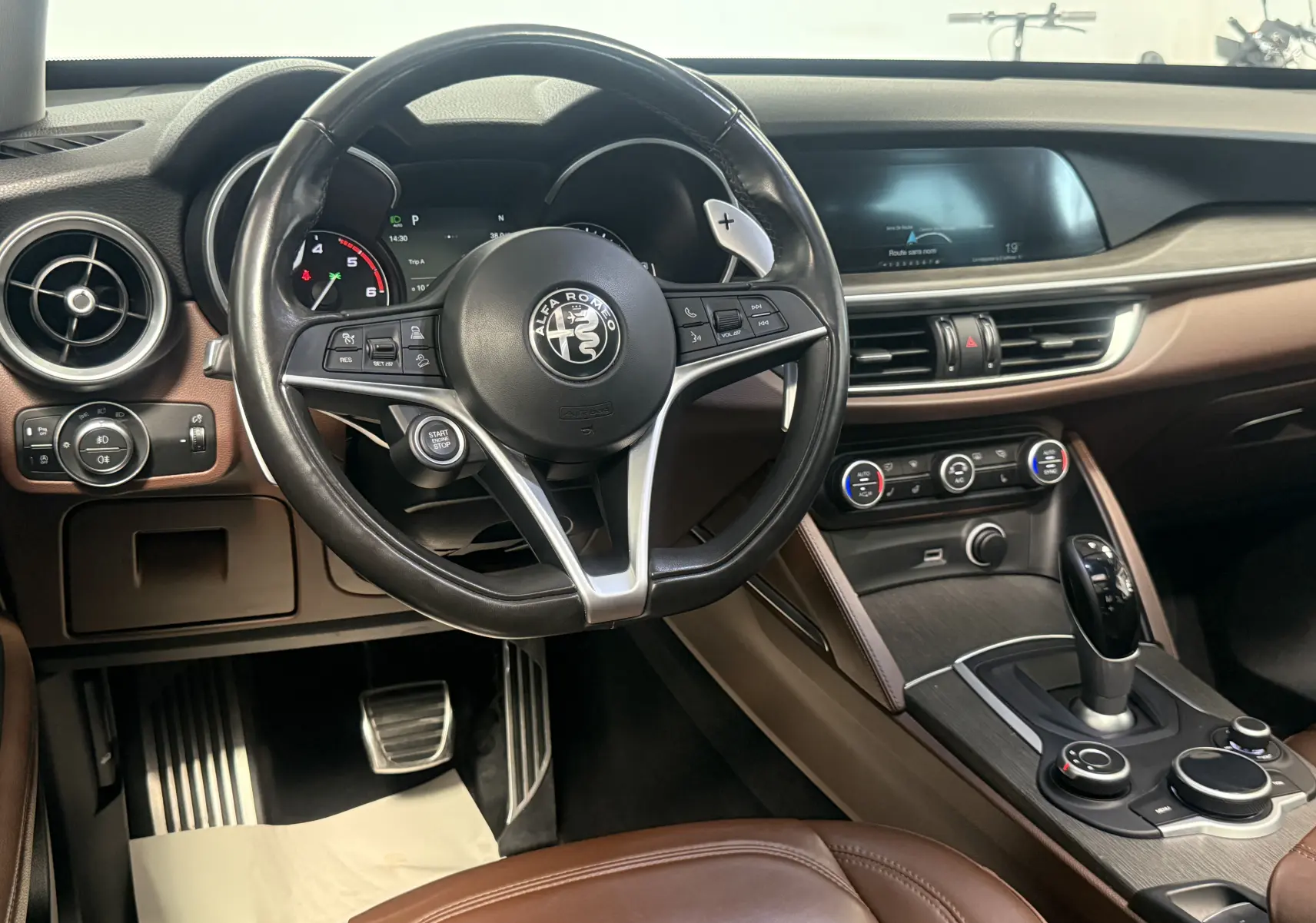 Vue intérieure côté conducteur de l'Alfa Romeo Stelvio 2017, volant cuir noir et tableau de bord marron avec écran digital.