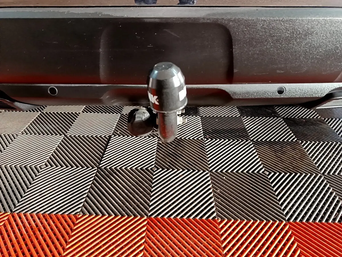 Gros plan sur l'attelage noir à l'arrière d'un Peugeot 3008 blanc, posé sur un sol à damiers noir et rouge.