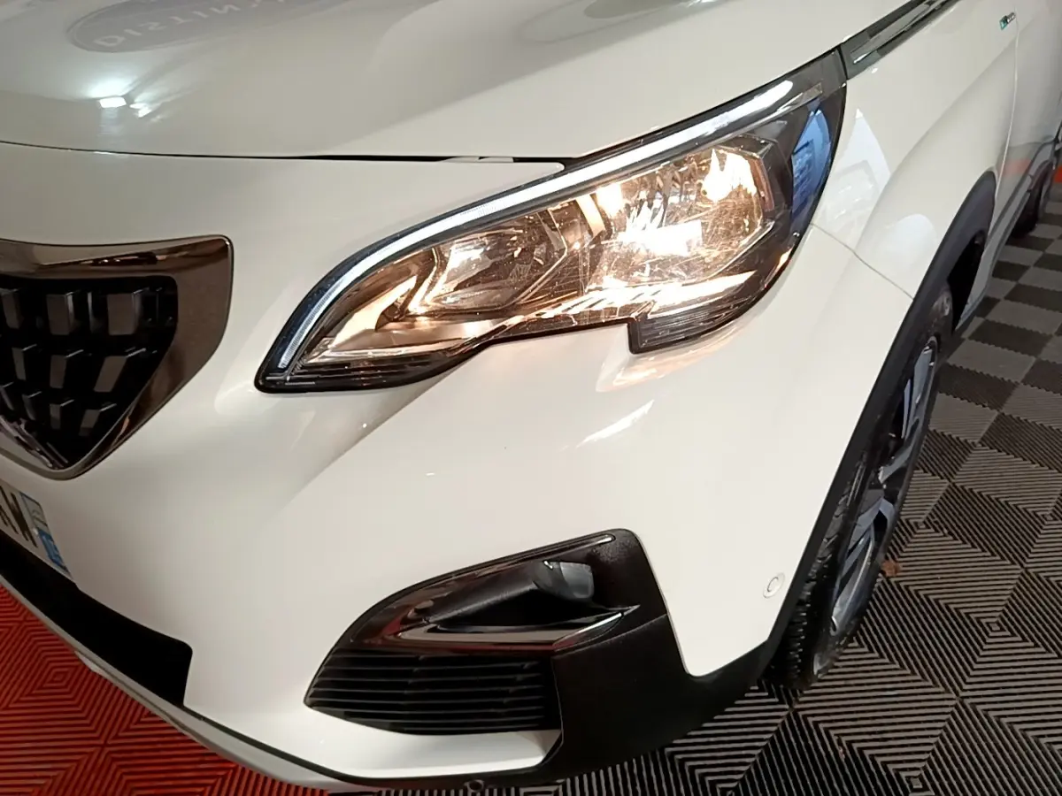 Gros plan sur l'avant droit blanc du Peugeot 3008 hybride, mettant en valeur le phare allumé et la calandre noire.