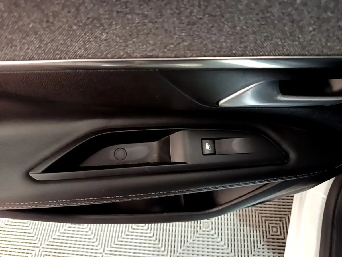 Gros plan sur la commande de lève-vitre côté gauche de la porte intérieure noire du Peugeot 3008 blanc hybride rechargeable.