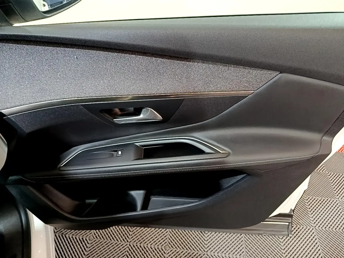 Vue intérieure côté gauche de la porte avant d'une Peugeot 3008 blanche avec garniture noire et poignée argentée.