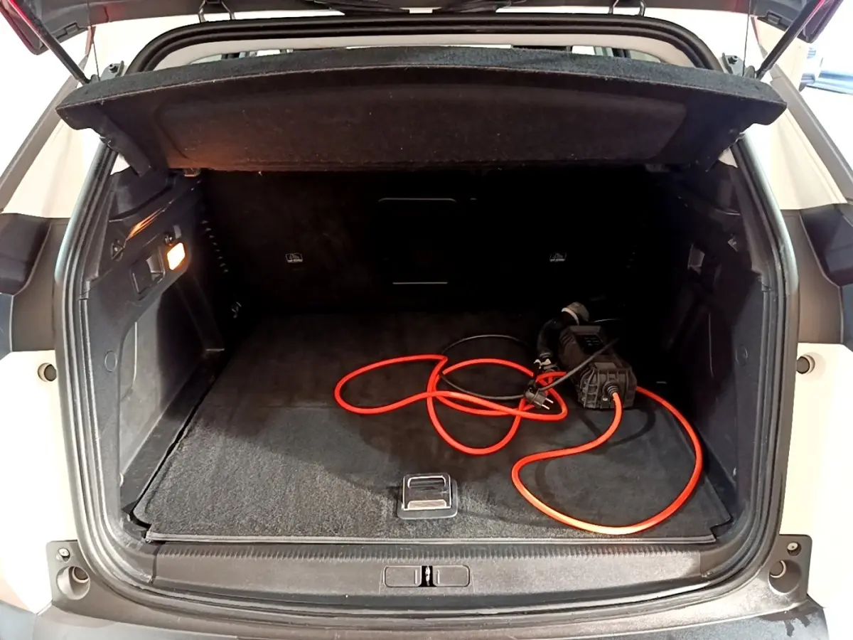 Coffre ouvert vu de l'arrière d'un Peugeot 3008 blanc avec câble de recharge hybride visible à l'intérieur.