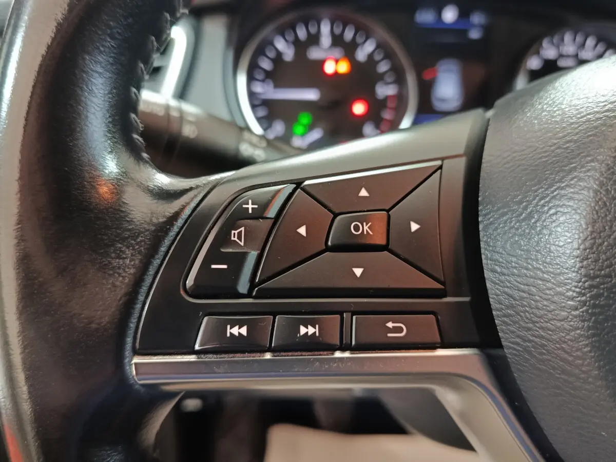 Gros plan sur les commandes multifonctions noires du volant cuir du Nissan Qashqai 2019, tableau de bord flou en arrière-plan.