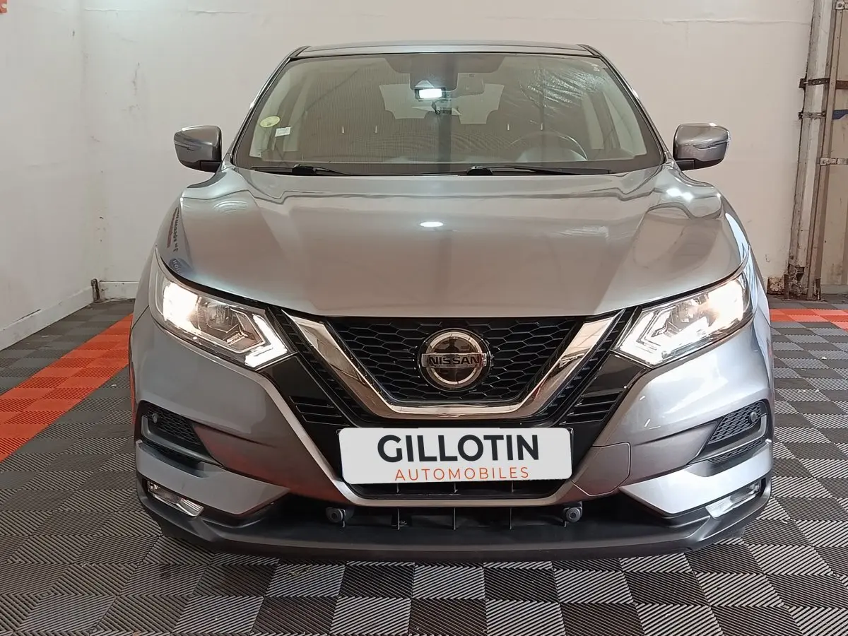 Vue frontale d'un Nissan Qashqai gris clair avec phares allumés et calandre chromée dans un garage.