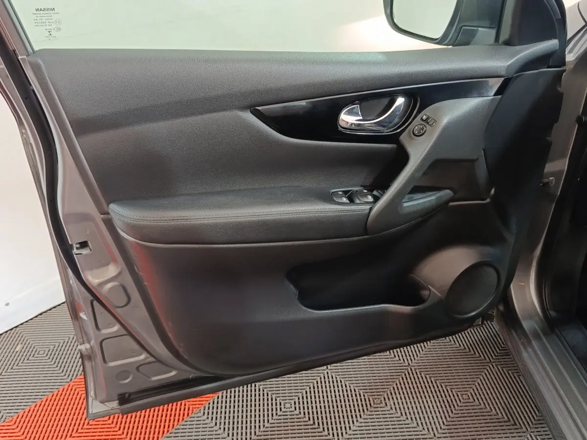 Porte avant gauche ouverte d'un Nissan Qashqai gris clair, montrant le panneau intérieur noir avec commandes électriques.