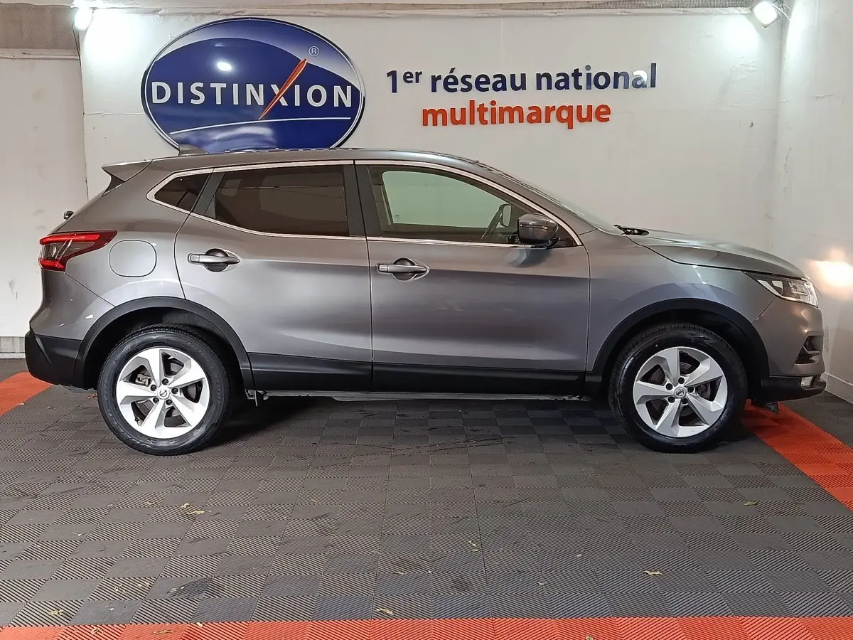 Profil côté gauche d'un Nissan Qashqai gris clair 2019 garé en intérieur avec jantes alliage et vitres teintées.