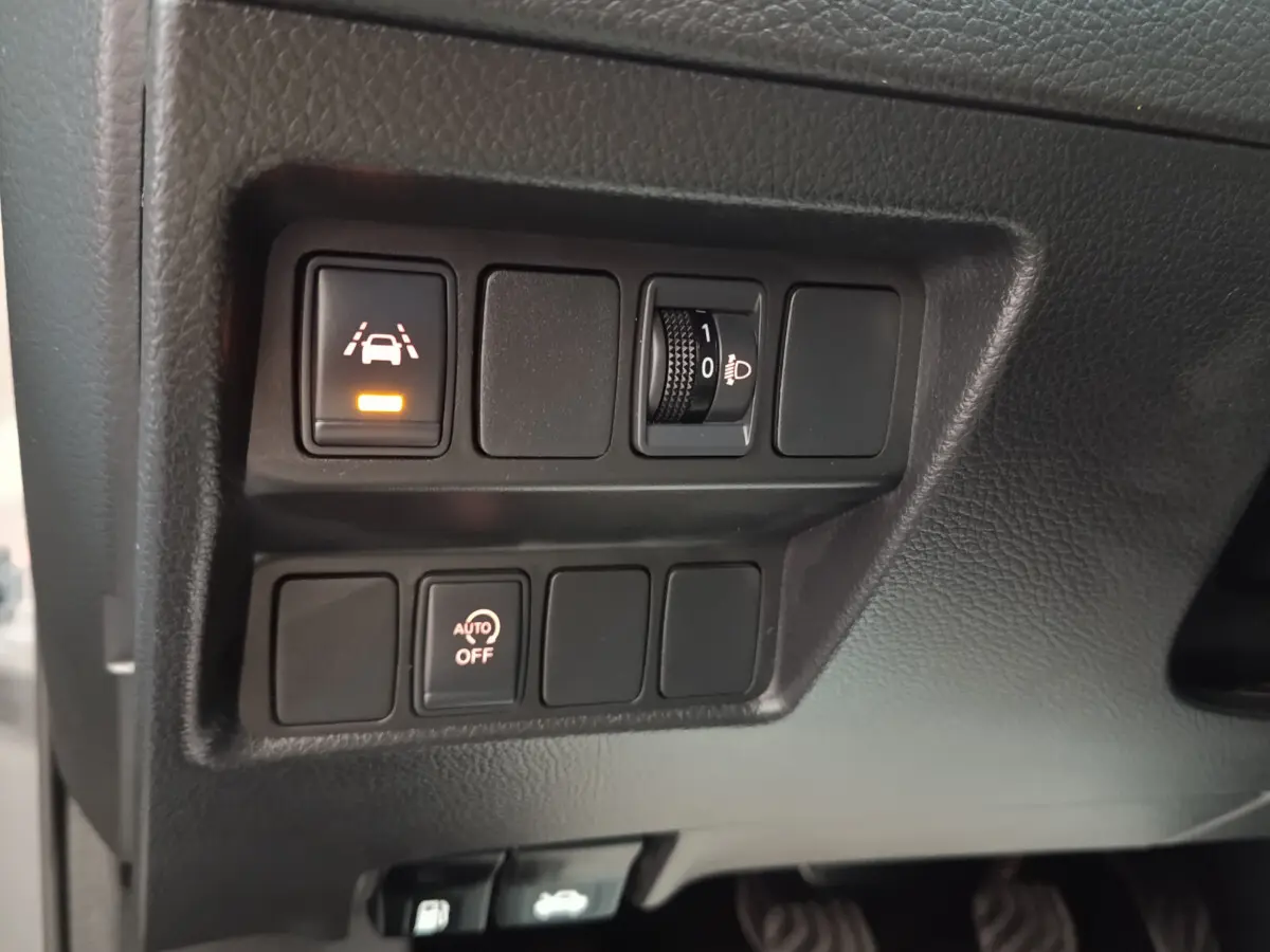Gros plan sur les commandes de réglage des phares et d'aide à la conduite du tableau de bord du Nissan Qashqai gris clair 2019.