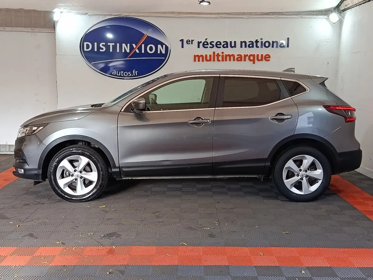 Profil côté gauche d'un Nissan Qashqai gris clair 2019 garé en intérieur avec jantes alliage et vitres teintées.