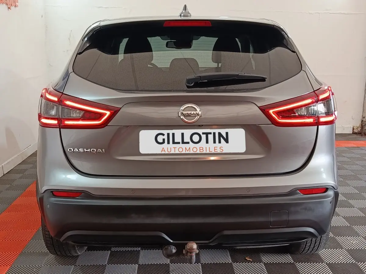 Vue arrière d'un Nissan Qashqai gris clair avec feux LED allumés et attelage visible dans un garage.