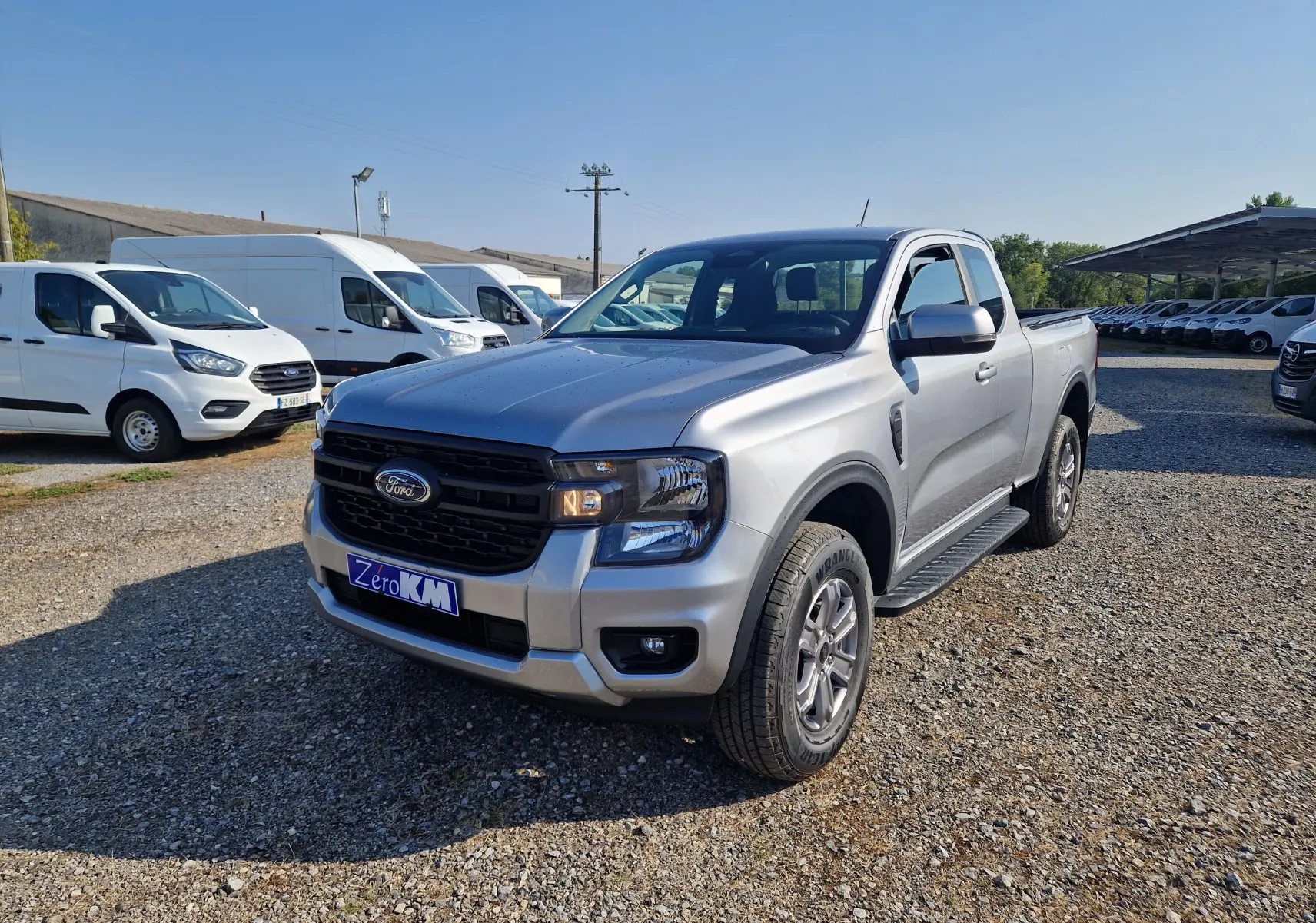 Ford Ranger Super Cabine gris iconic en 3/4 avant droit, avec calandre noire et plaque Zero KM visible.