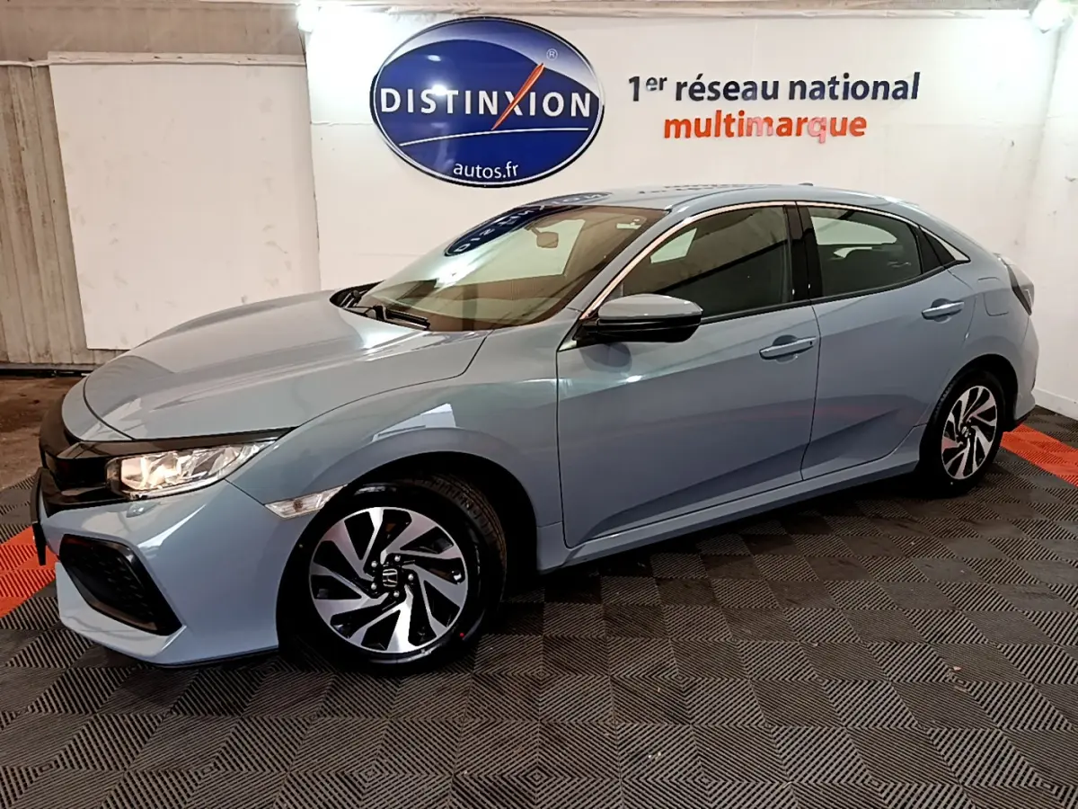 Vue 3/4 avant droit d'une Honda Civic gris clair avec jantes noires et blanches, stationnée en intérieur showroom.