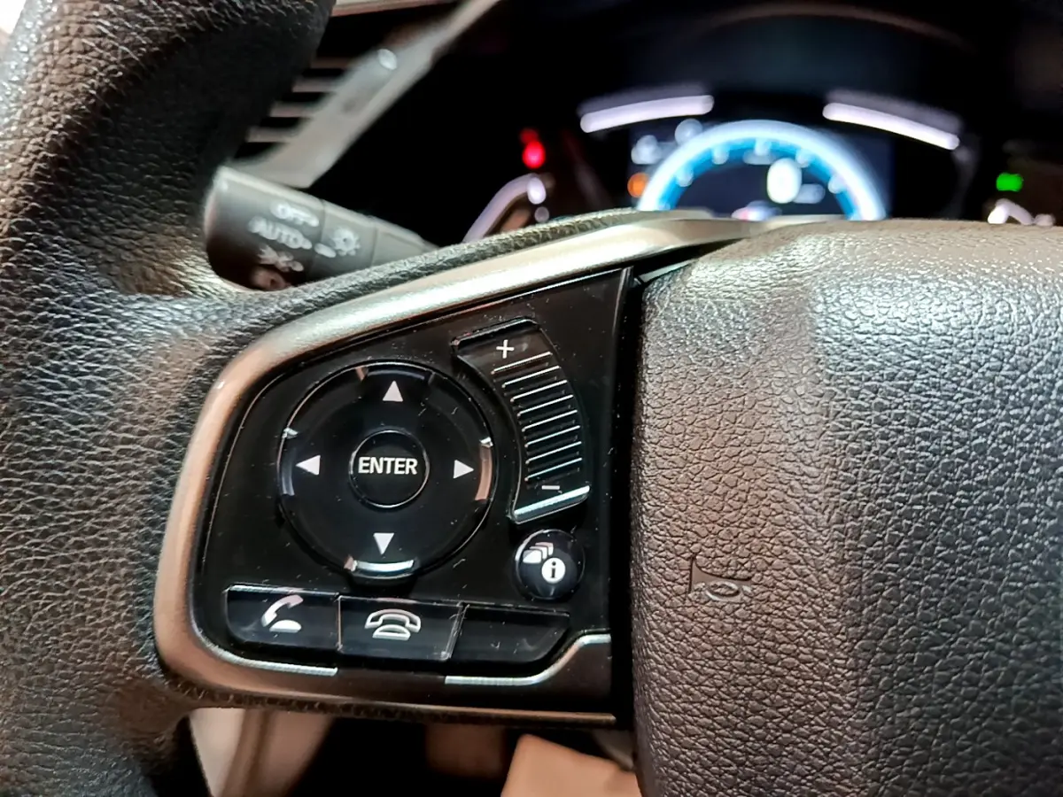 Gros plan sur les commandes gauche du volant cuir de la Honda Civic 1.0 i-VTEC Exclusive 2020, tableau de bord éclairé.